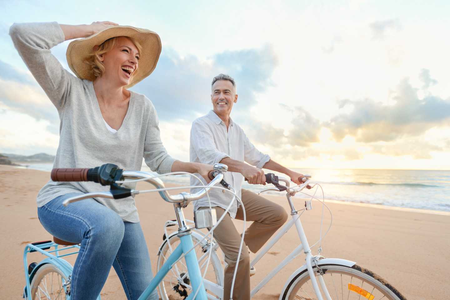 an elderly couple rides bicycles on the beach