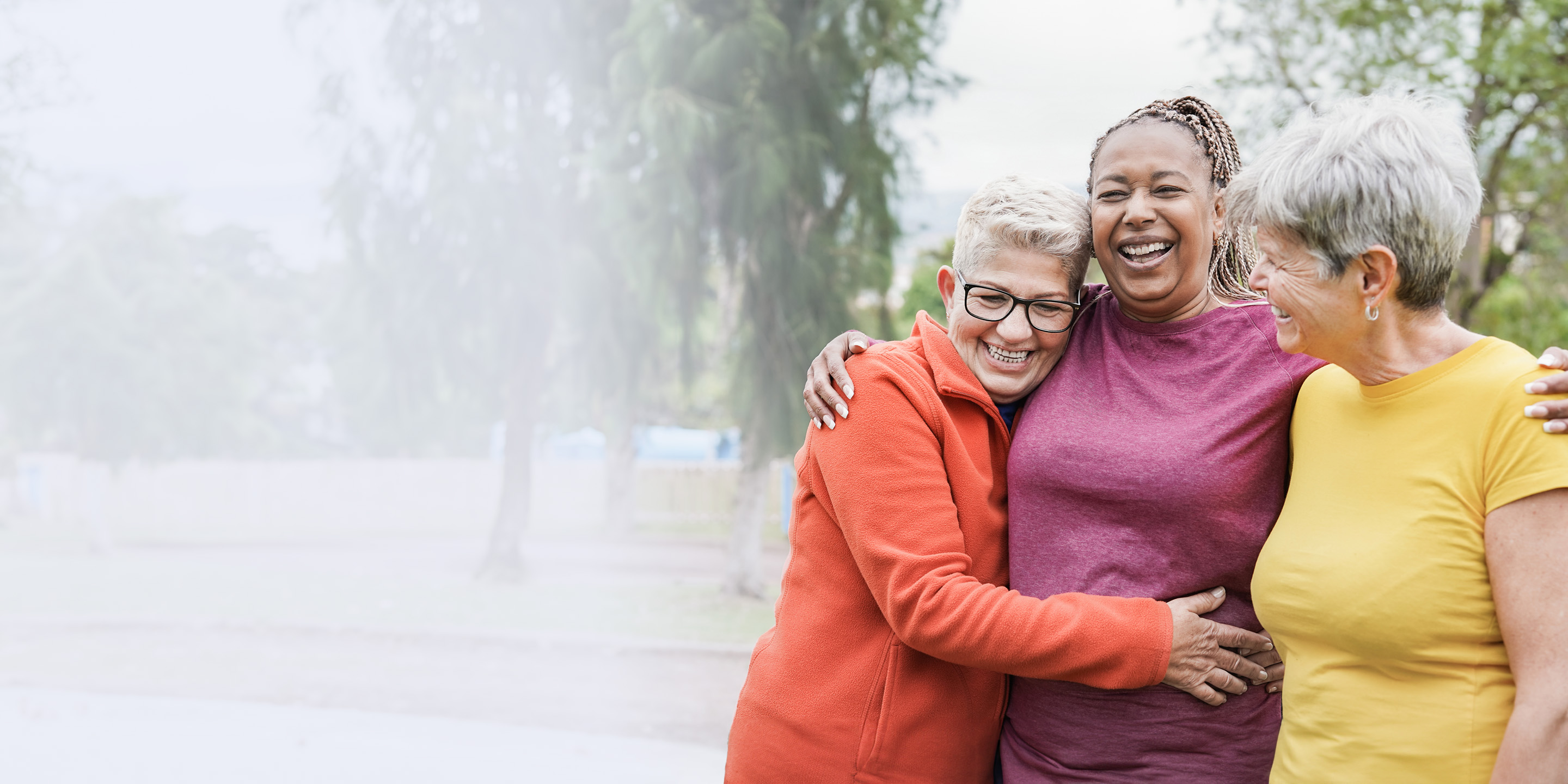 a trio of elderly women go walking on park trail and hug, smiling