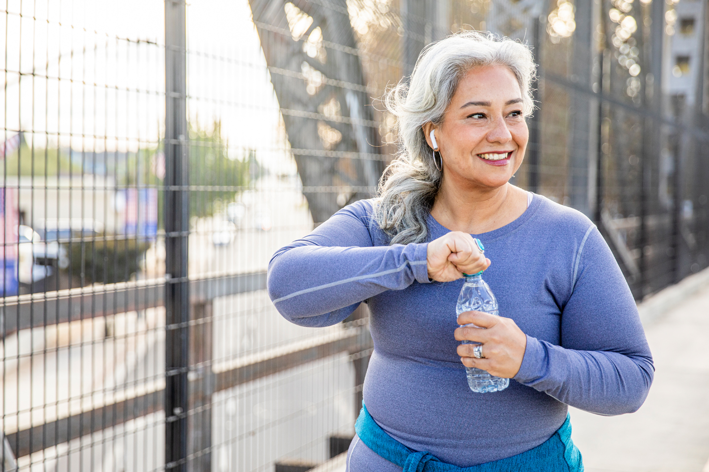an elderly woman walks on bridge with water bottle